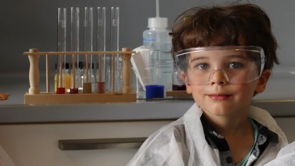 Like a real researcher: 5-year-old Vincent in the lab (Photo: THI). KiGa-Kind in einem Labor mit Schutzbrille und -Kleidung, im Hintergrund Reagenzgläser