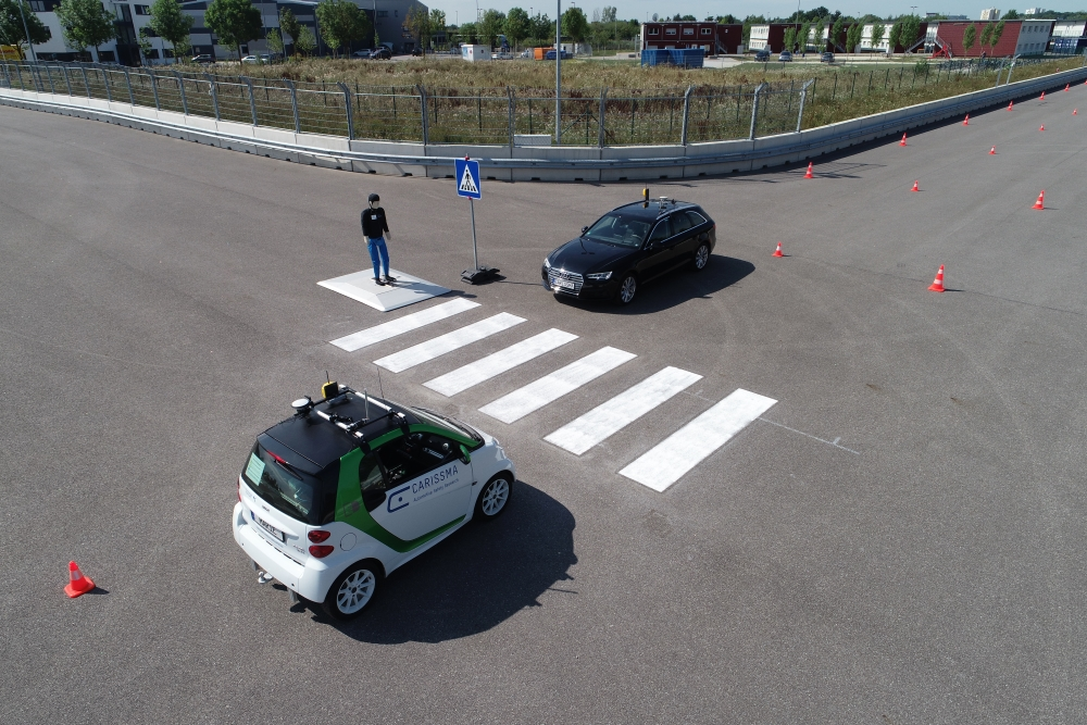 Abbildung von zwei Testfahrzeugen (Smart und Audi) an einem Zebrastreifen und einem Fußgängerdummy